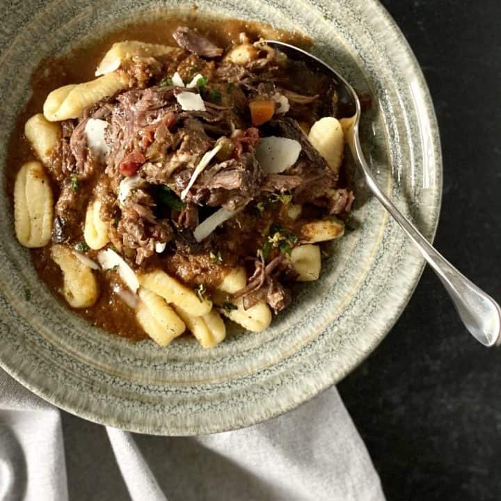 grey bowl filled with gnocchi and braised short ribs on grey napkin