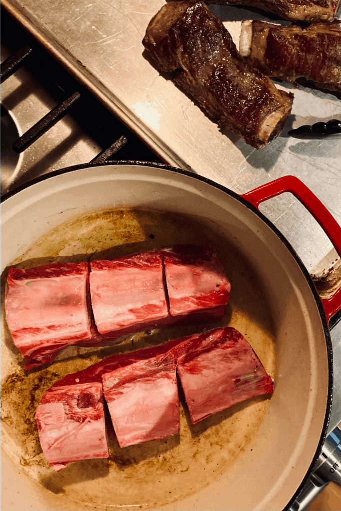 braising short ribs in dutch oven next to already browned short ribs on baking sheet