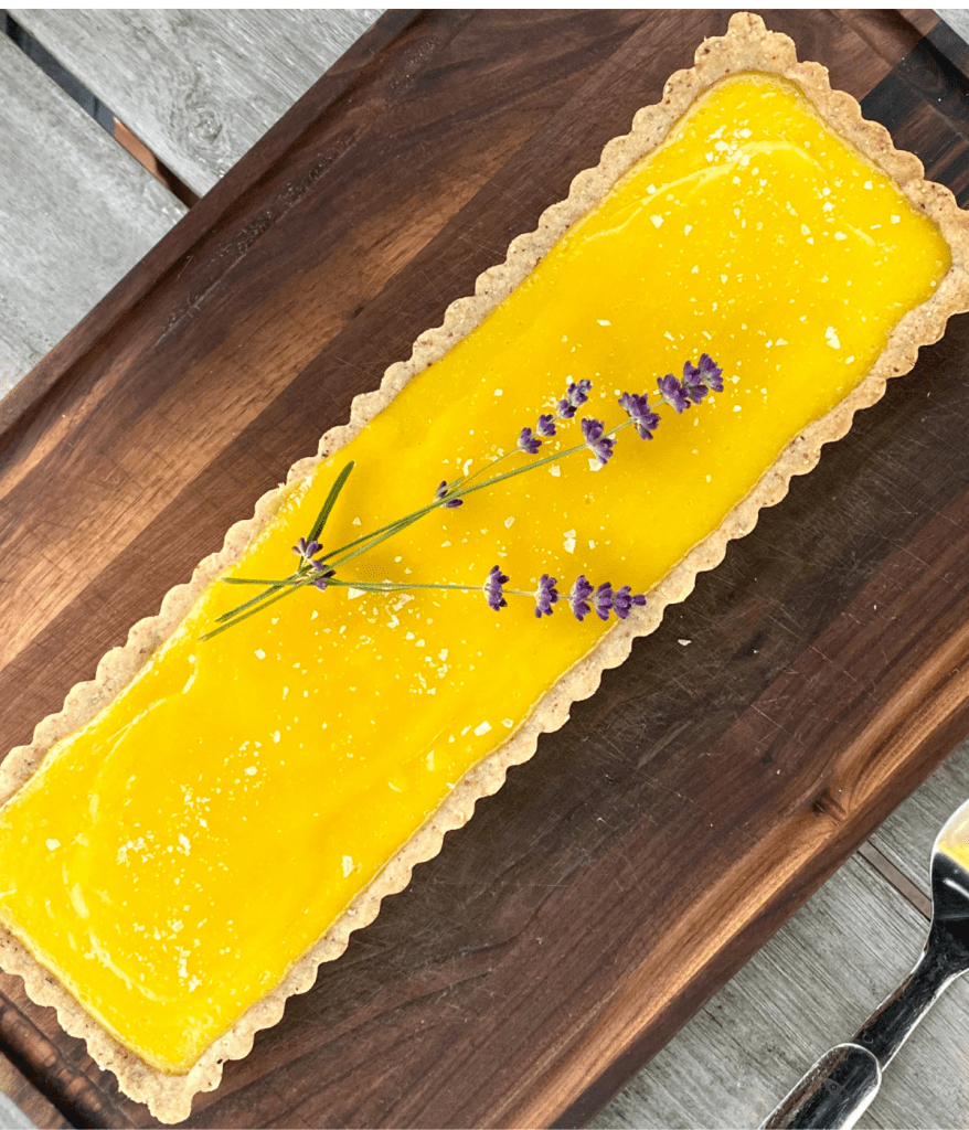 rectangular Lemon Tart With Almond Crust topped with fresh lavender sprigs on wood cutting board