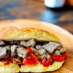 steak and peppers inside bun on wooden plate