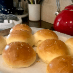 8 baked buns on parchment paper in front of red tea kettle