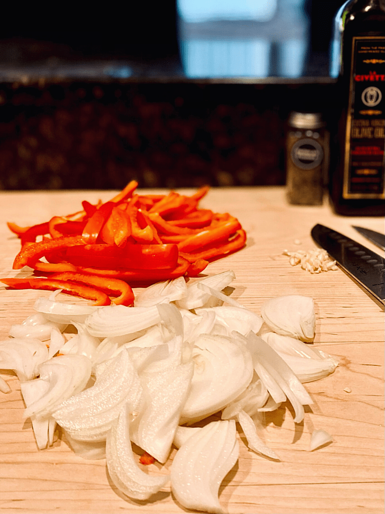 sliced red bell peppers onions and chopped garlic on wood cutting board