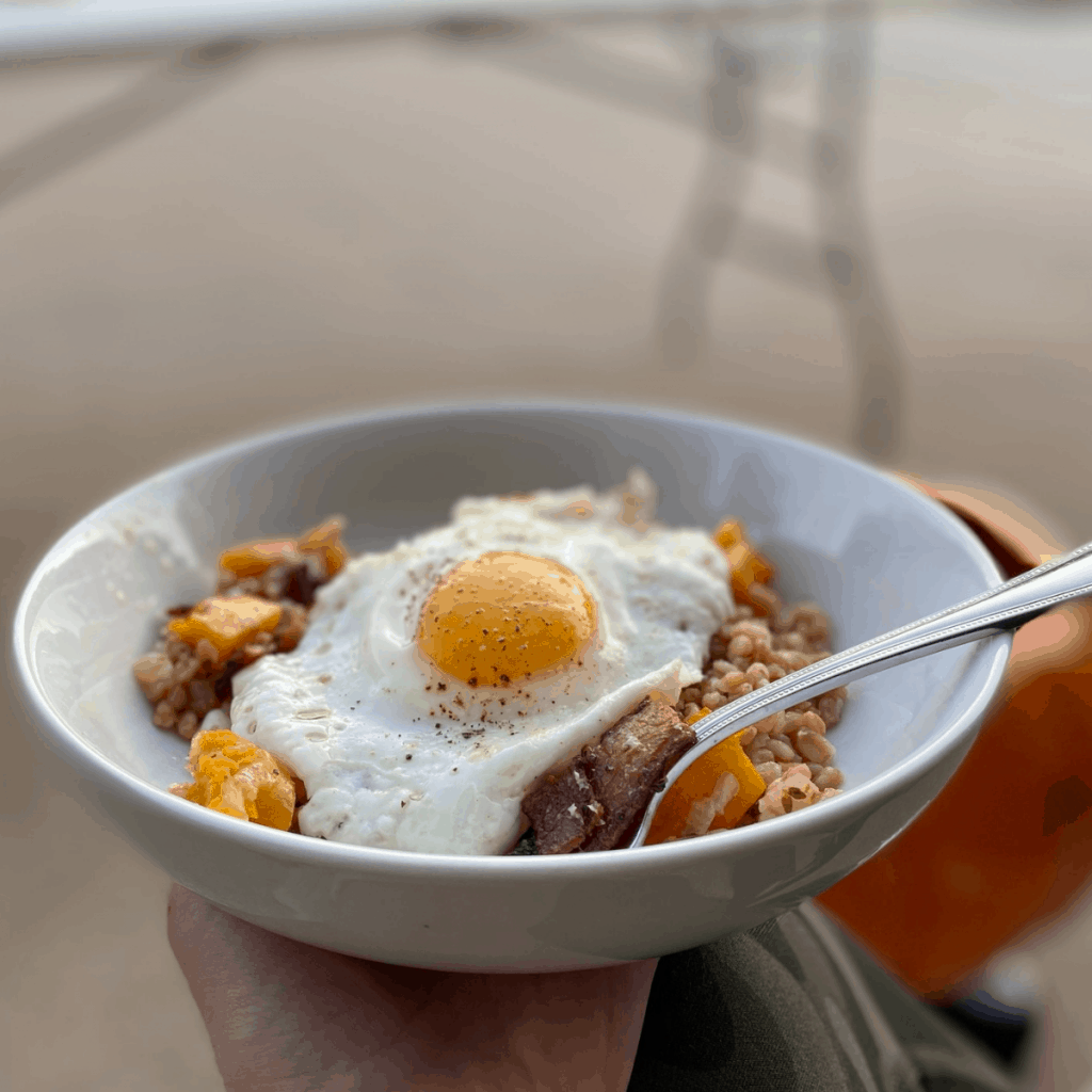 white bowl with farro and squash bake topped with a fried egg