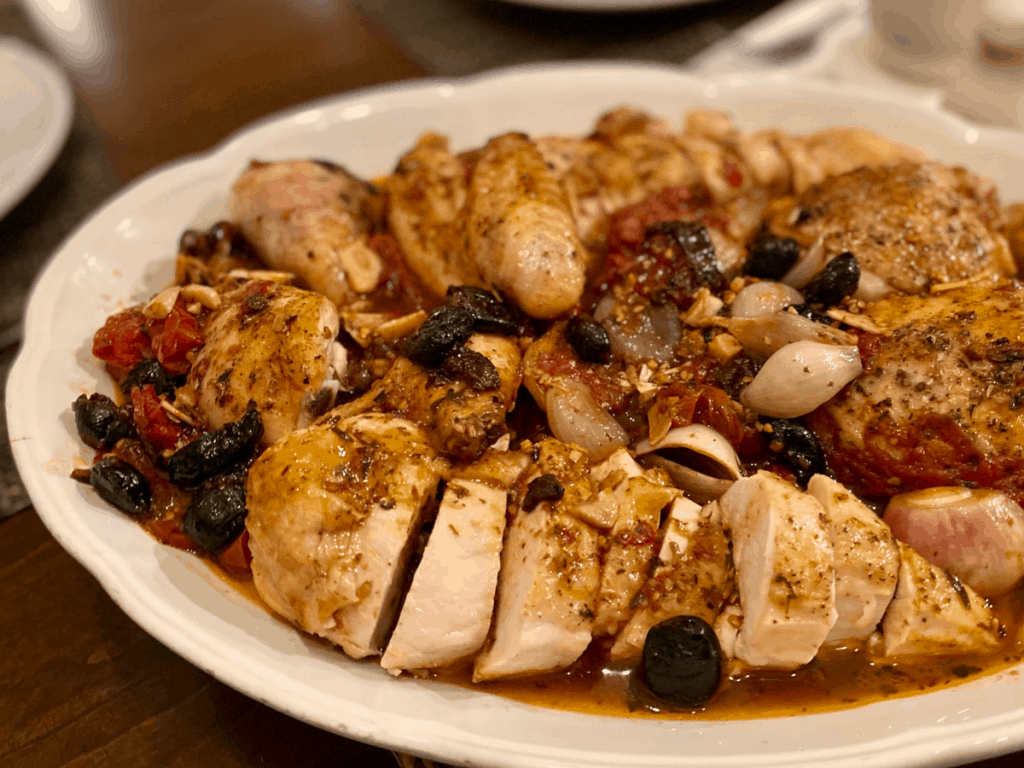 cut up chicken with tomatoes and olives on white oval platter