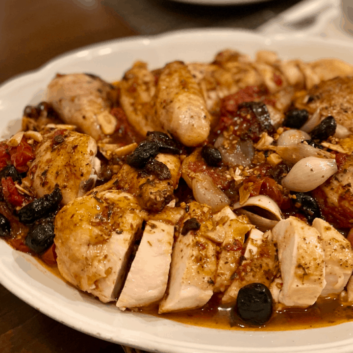 cut up chicken with tomatoes and olives on white oval platter