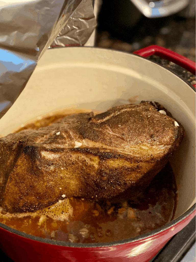 cooked pork shoulder with juices in red dutch oven