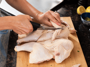 womans hands snipping wing tips from raw chicken with kitchen sheers on wood cutting board