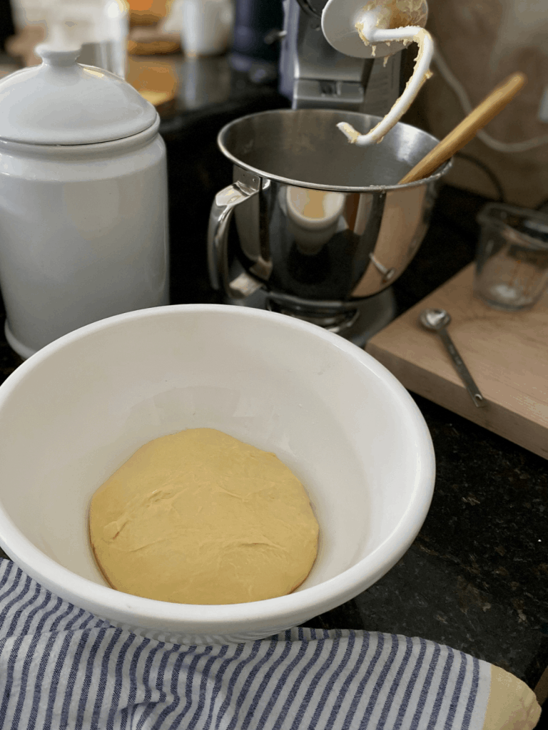 dough in white bowl in front of mixer with blue striped towell