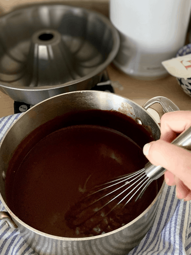whisking chocolate and butter in saucepan set on blue and white towel