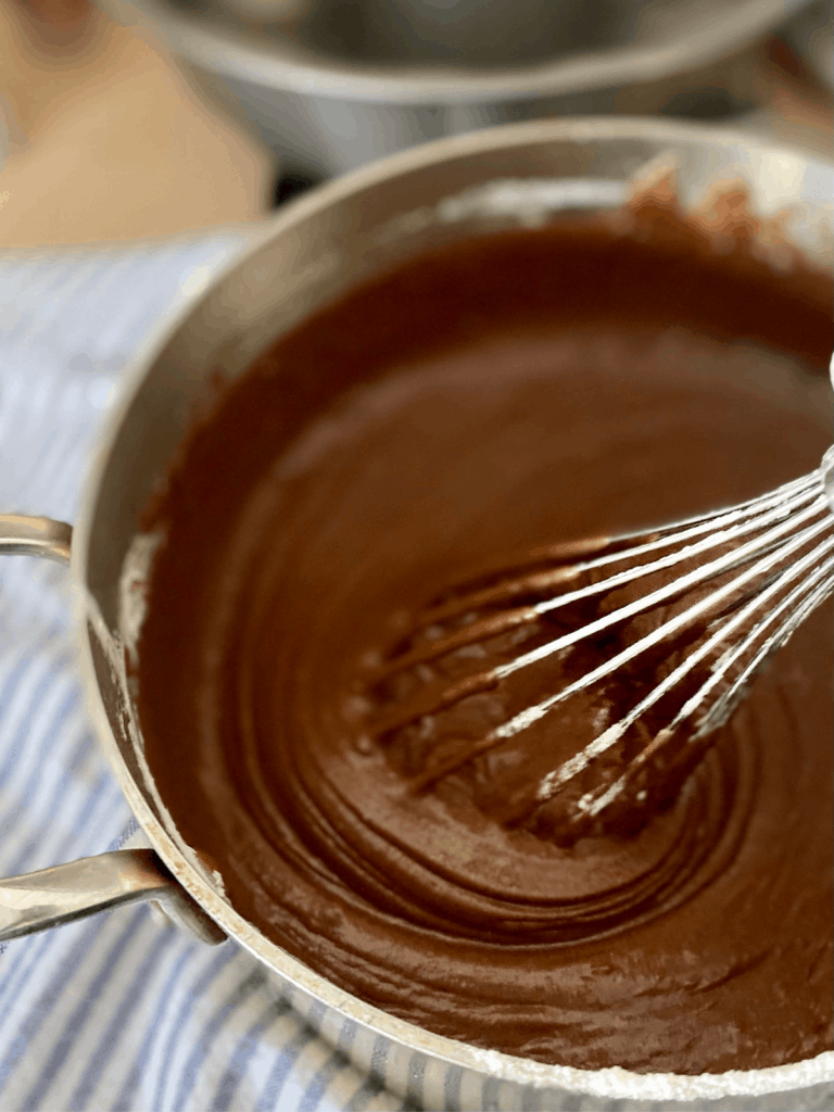 whisking smooth chocolate batter in saucepan on blue and white towel