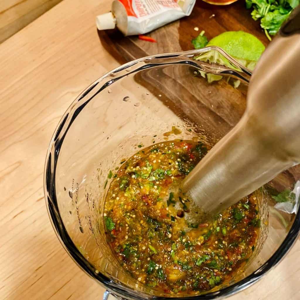 salsa ingredients being blended in clear pitcher with immersion blender