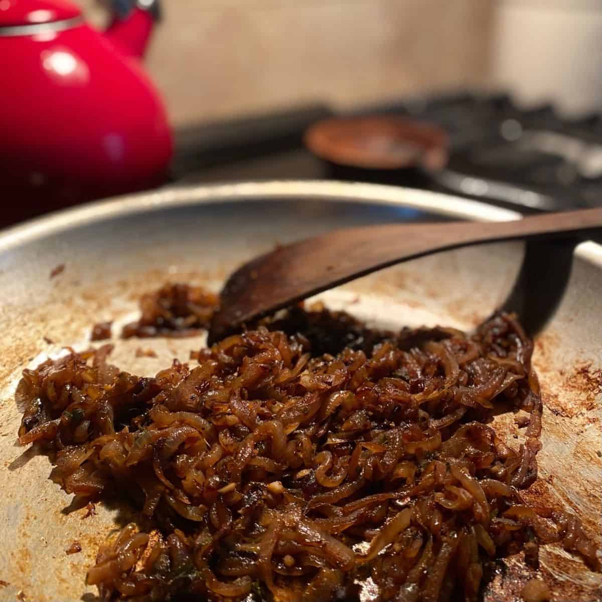 onions cooking in pan with wooden utensil