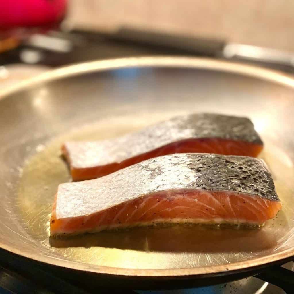 two pieces of salmon being seared in hot skillet