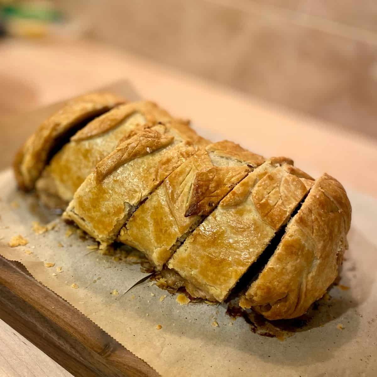 Baked, sliced beef wellington on parchment lined wood board