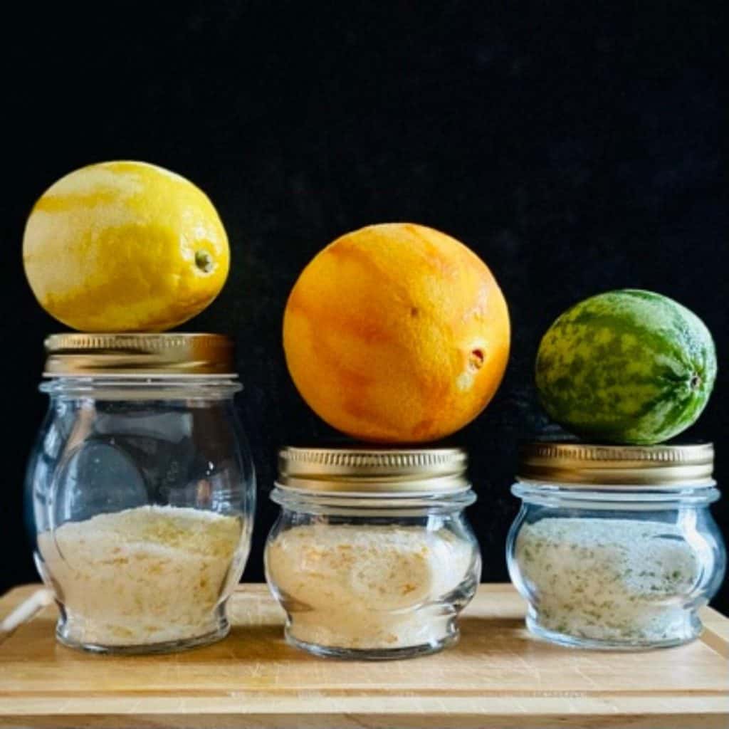 3 jars of citrus salt with zested piece of fruit on top of each