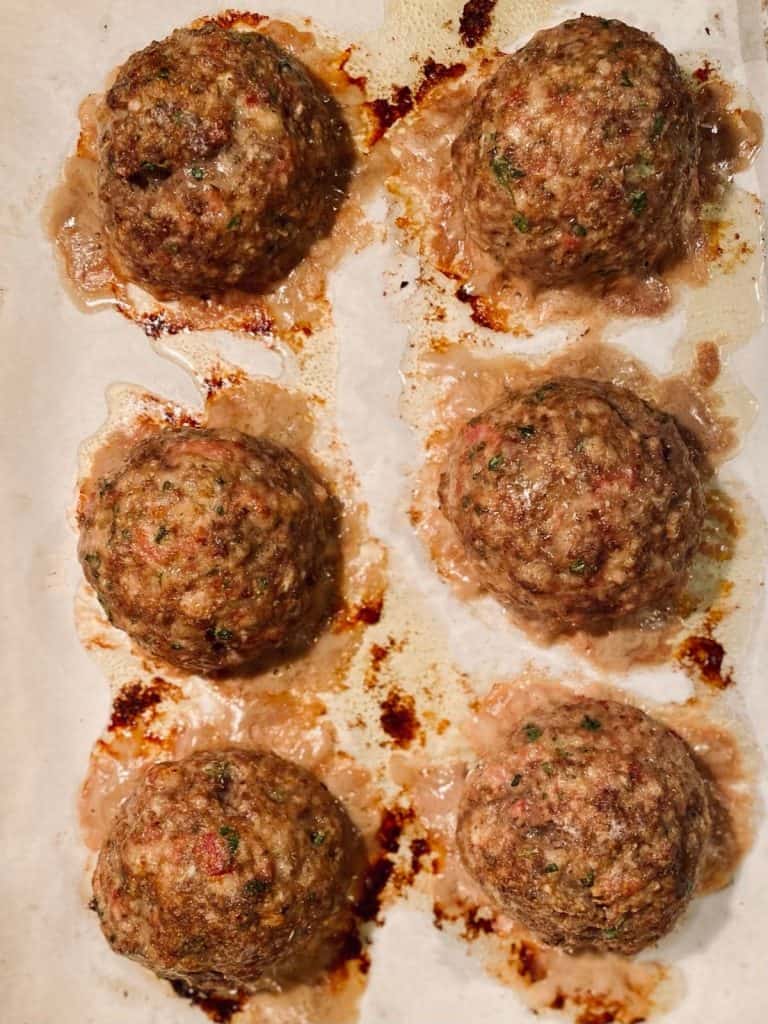 6 cooked meatballs on parchment lined baking sheet