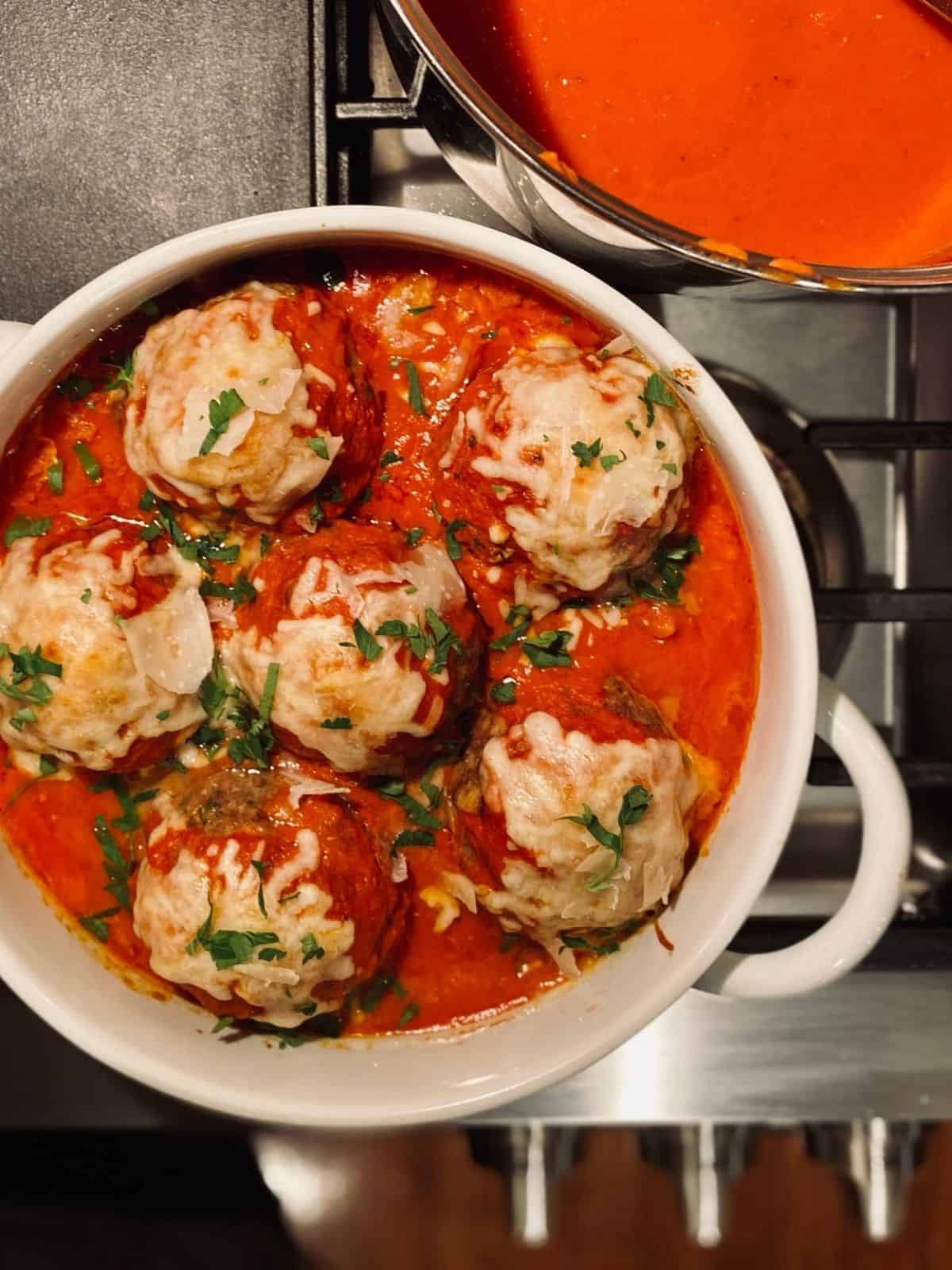 baked meatballs in sauce topped with cheese and parsley in round white casserole dish