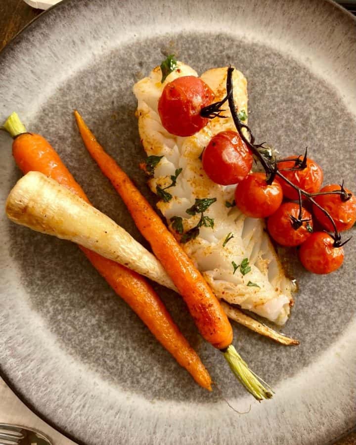 broiled cod and stem tomatoes with roasted root vegetables on grey plate