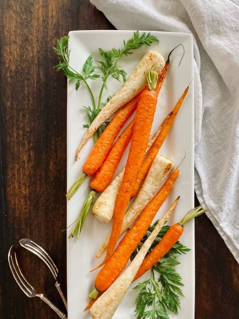 long, white platter with roasted carrots & parsley root garnished with carrot top fronds