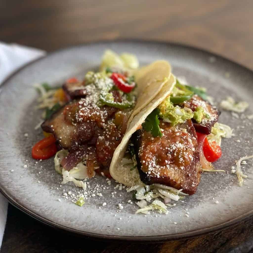 2 pork belly tacos on grey plate