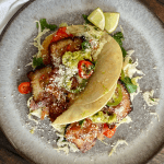 2 pork belly tacos on grey plate with white napkin