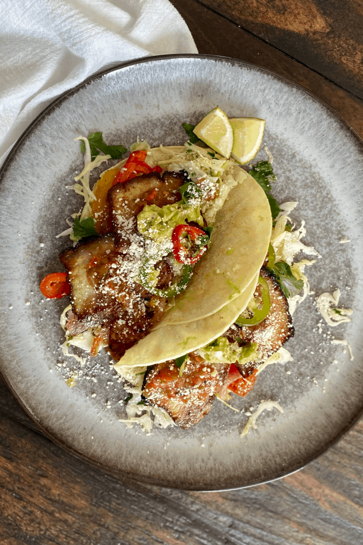 2 pork belly tacos on grey plate with white napkin