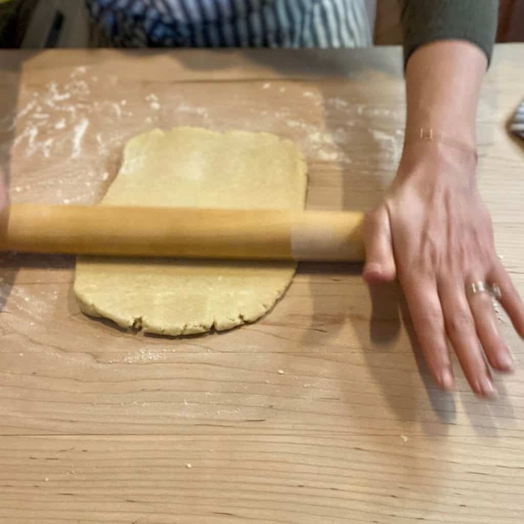 dough on wood counter being rolled out with wooden rolling pin