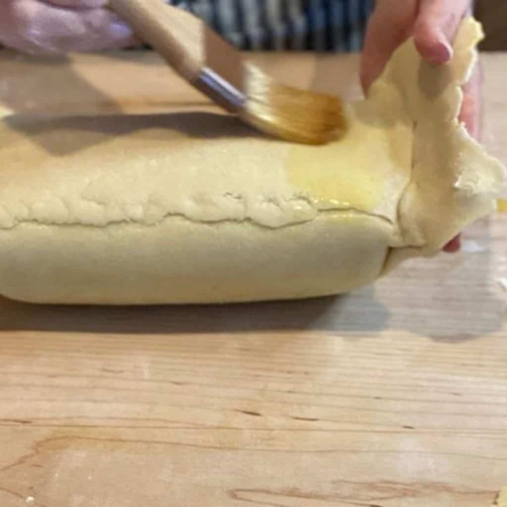 dough wrapped wellington being brushed with egg wash