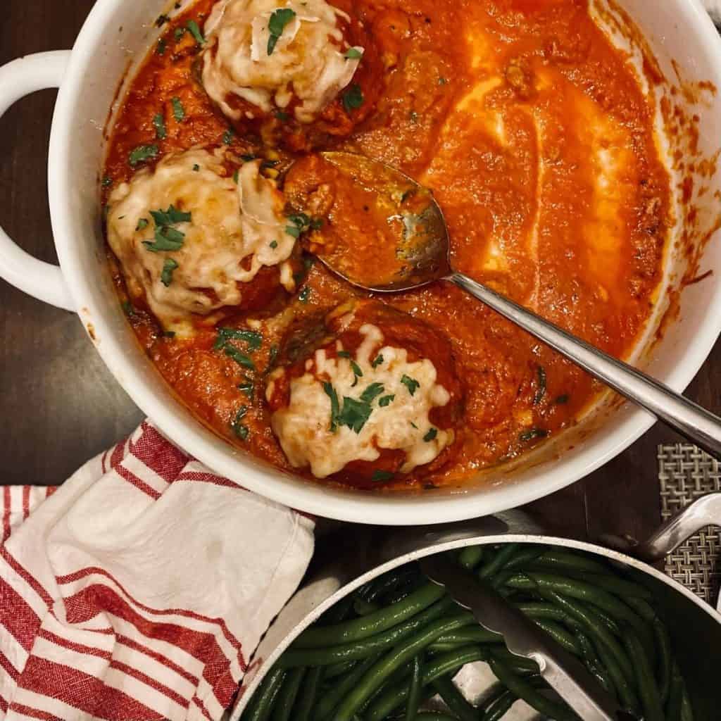 round casserole with serving spoon and 3 meatballs and sauce left