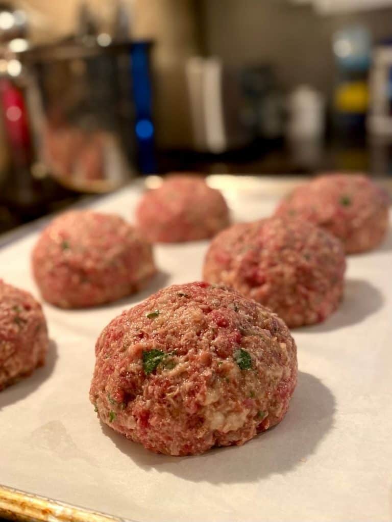 6 uncooked meatballs on parchment lined baking sheet