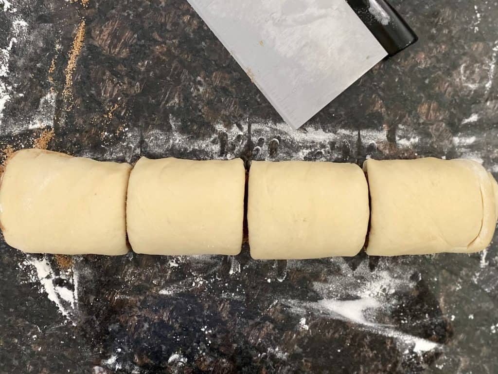 rolled up dough cut into four sections next to bench scraper on floured counter