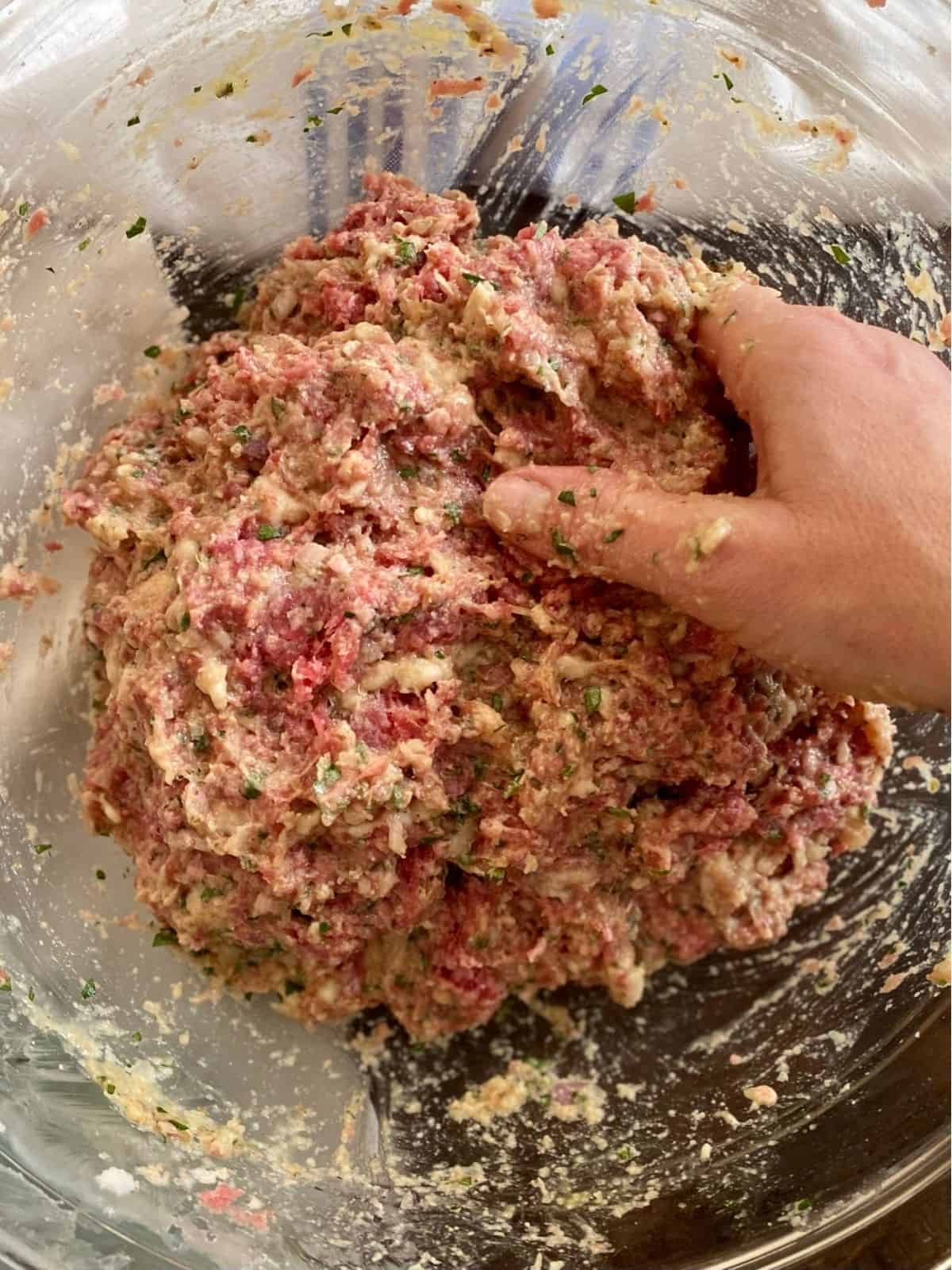 hand mixing final meatball mixture in glass bowl