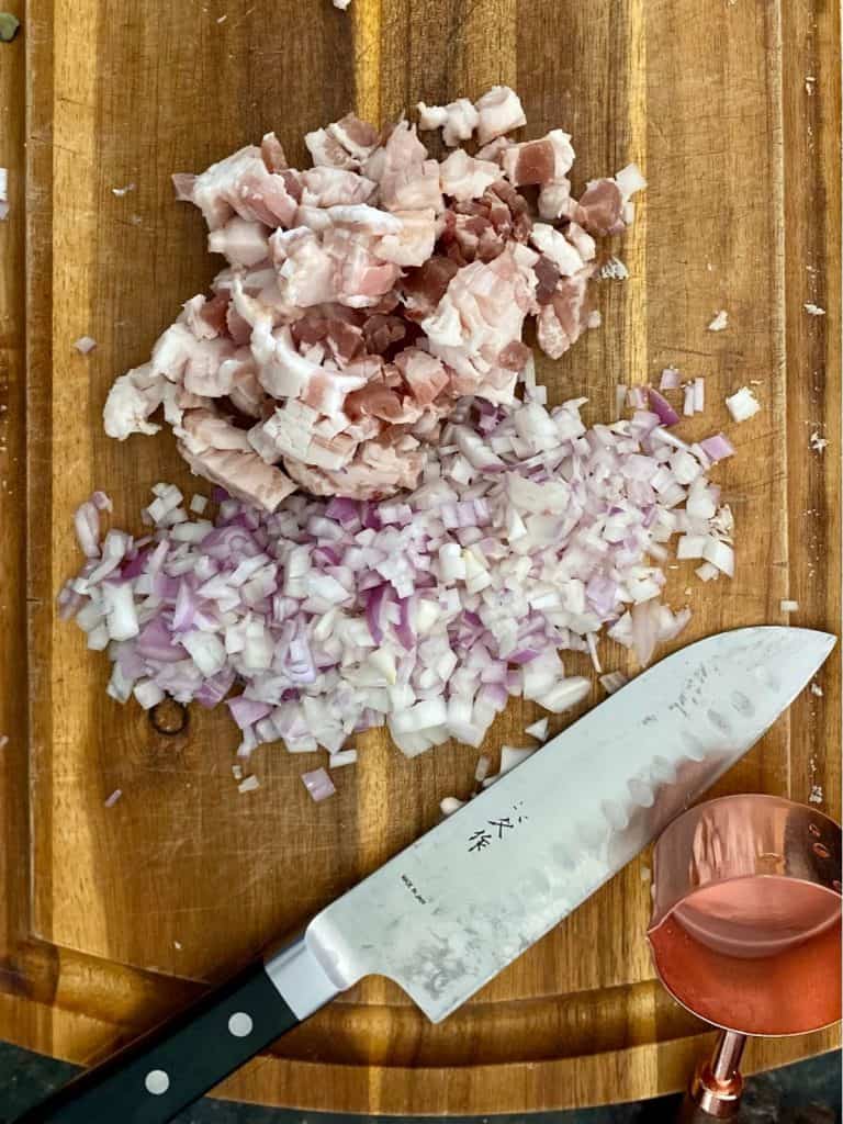 cutting board with diced shallot and diced bacon next to knife and measuring cup