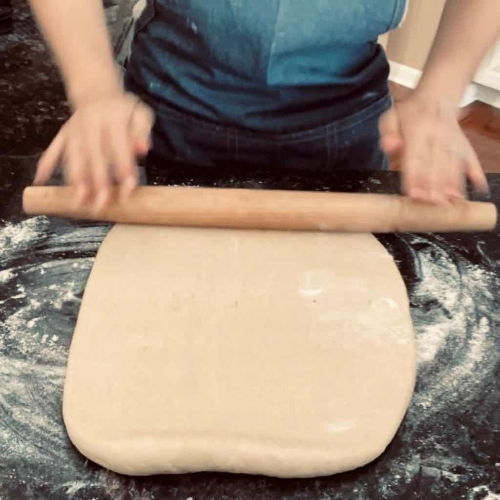 dough on counter being rolled out with wooden rolling pin