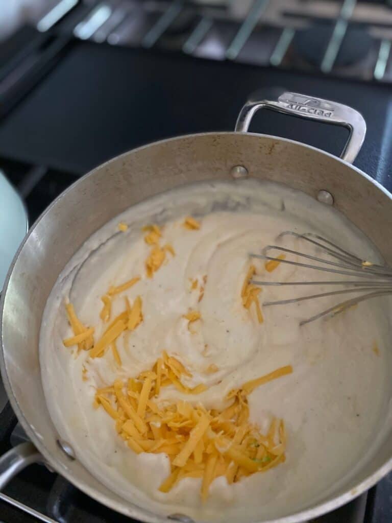 sauce pan on stove top with cheese being whisked into béchamel sauce
