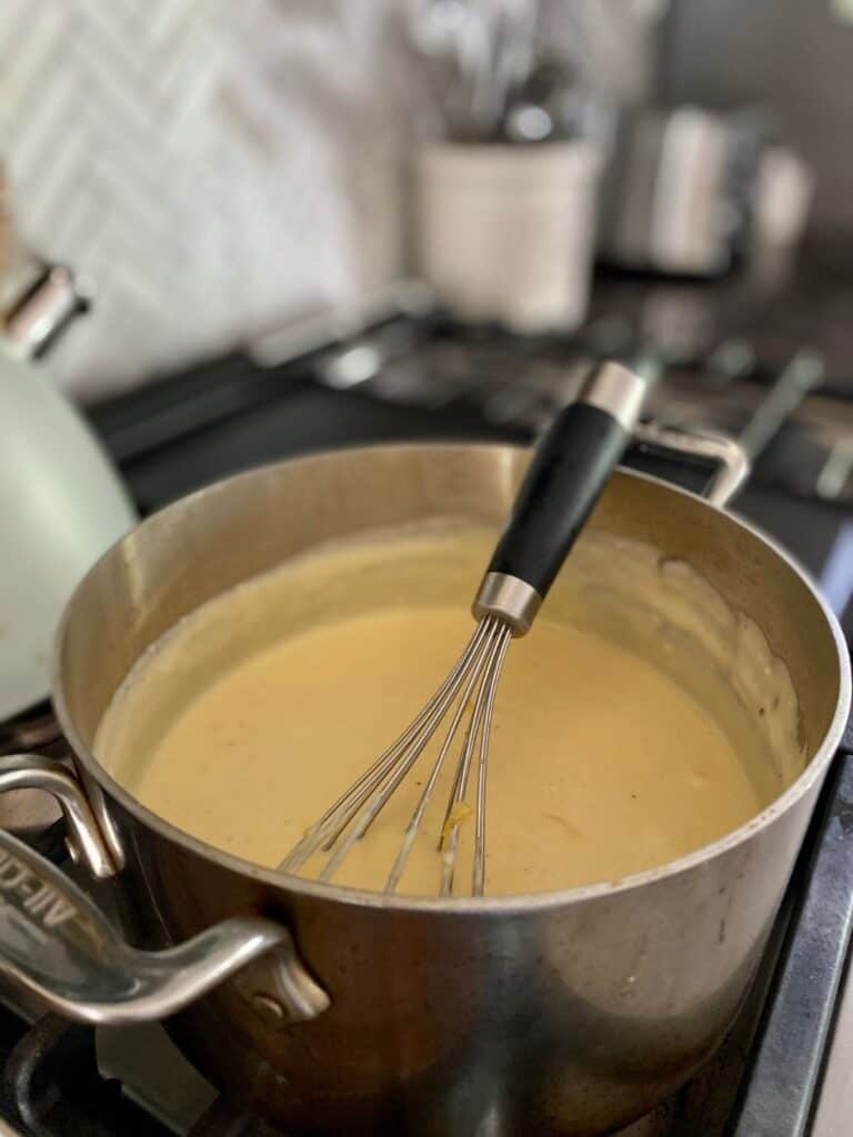 saucepan with whisk on stove top filled with finished cheese sauce