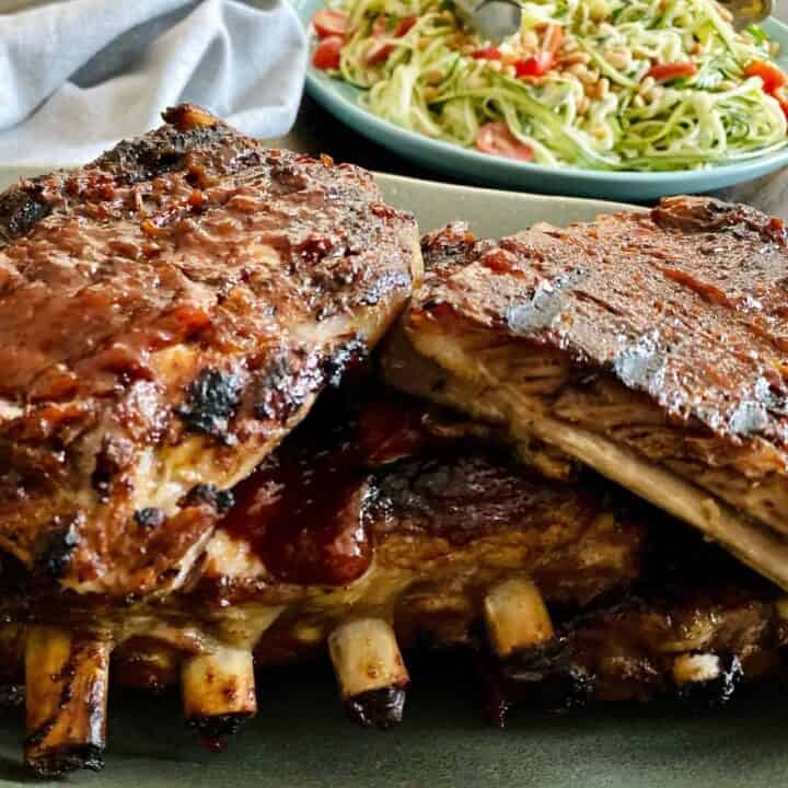 close up of plated bbq ribs with zucchini salad in background