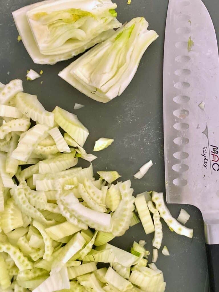 sliced and quartered fennel on cutting board next to knife