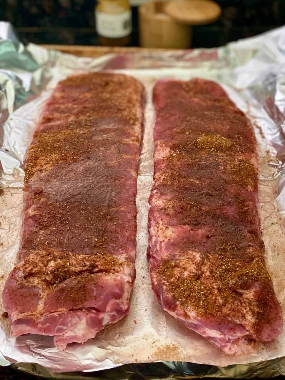 two slabs of uncooked, seasoned ribs on foil lined pan