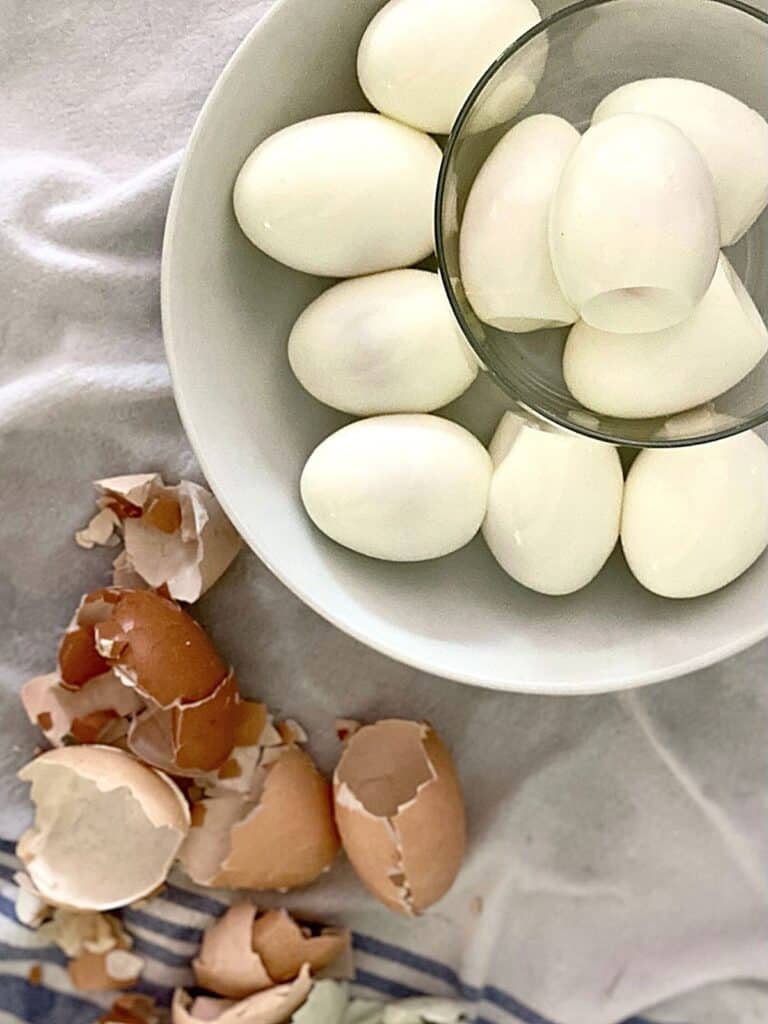 peeled eggs in bowl next to eggshells