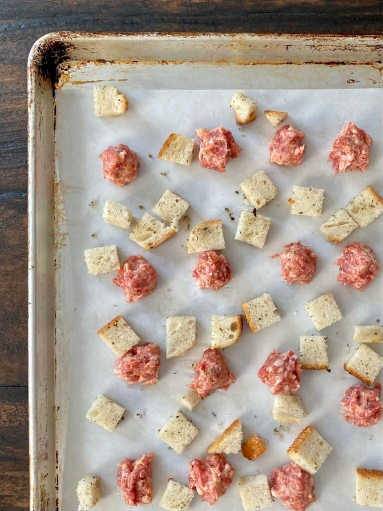 uncooked sausage and bread cubes on baking sheet