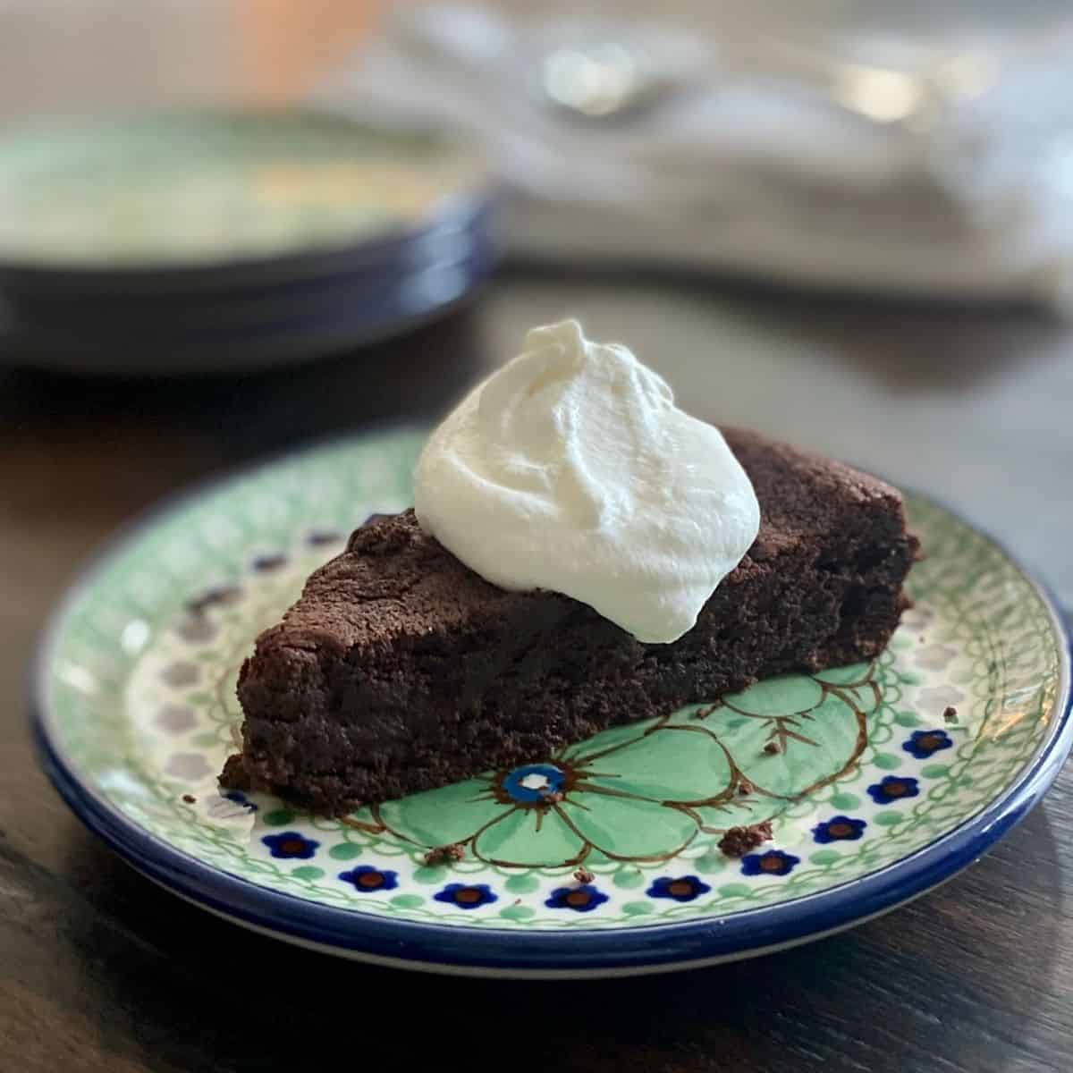 Almost Flourless bittersweet chocolate Cake with whipped cream on blue and green plate