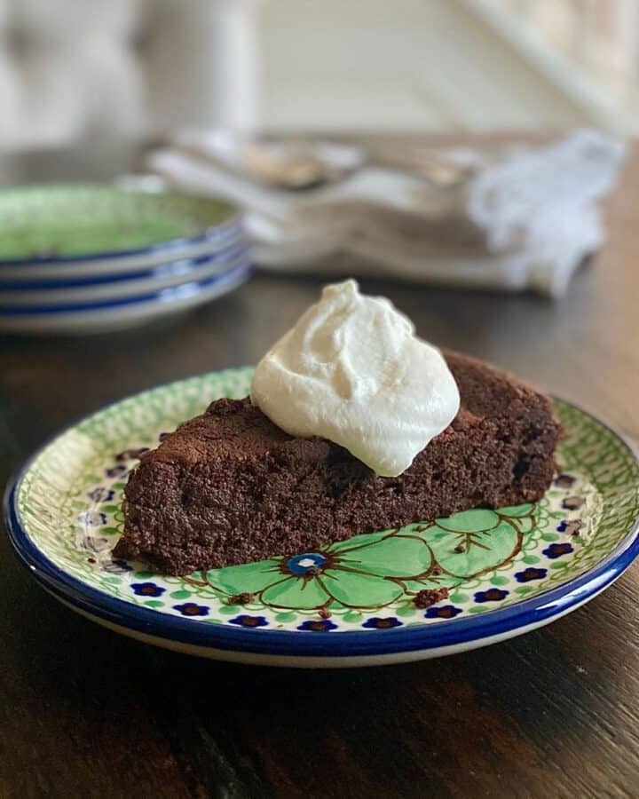 Almost flourless bittersweet chocolate cake with whipped cream on blue and green plate
