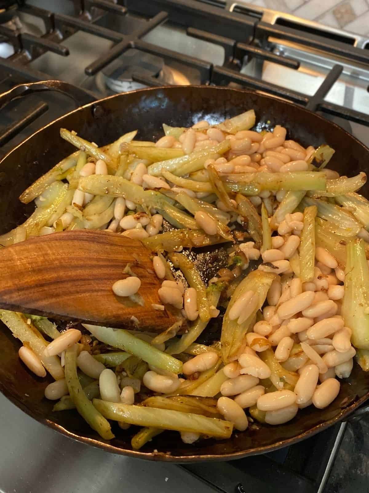 stirring beans into cooked fennel with wooden spatula on stove top
