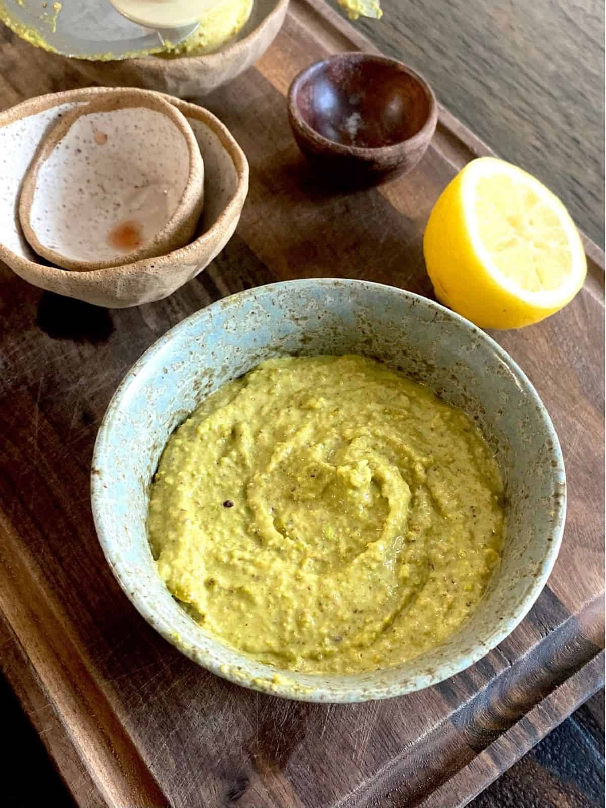bowl of pistachio butter on wood board in front of empty bowls and squeezed lemon half