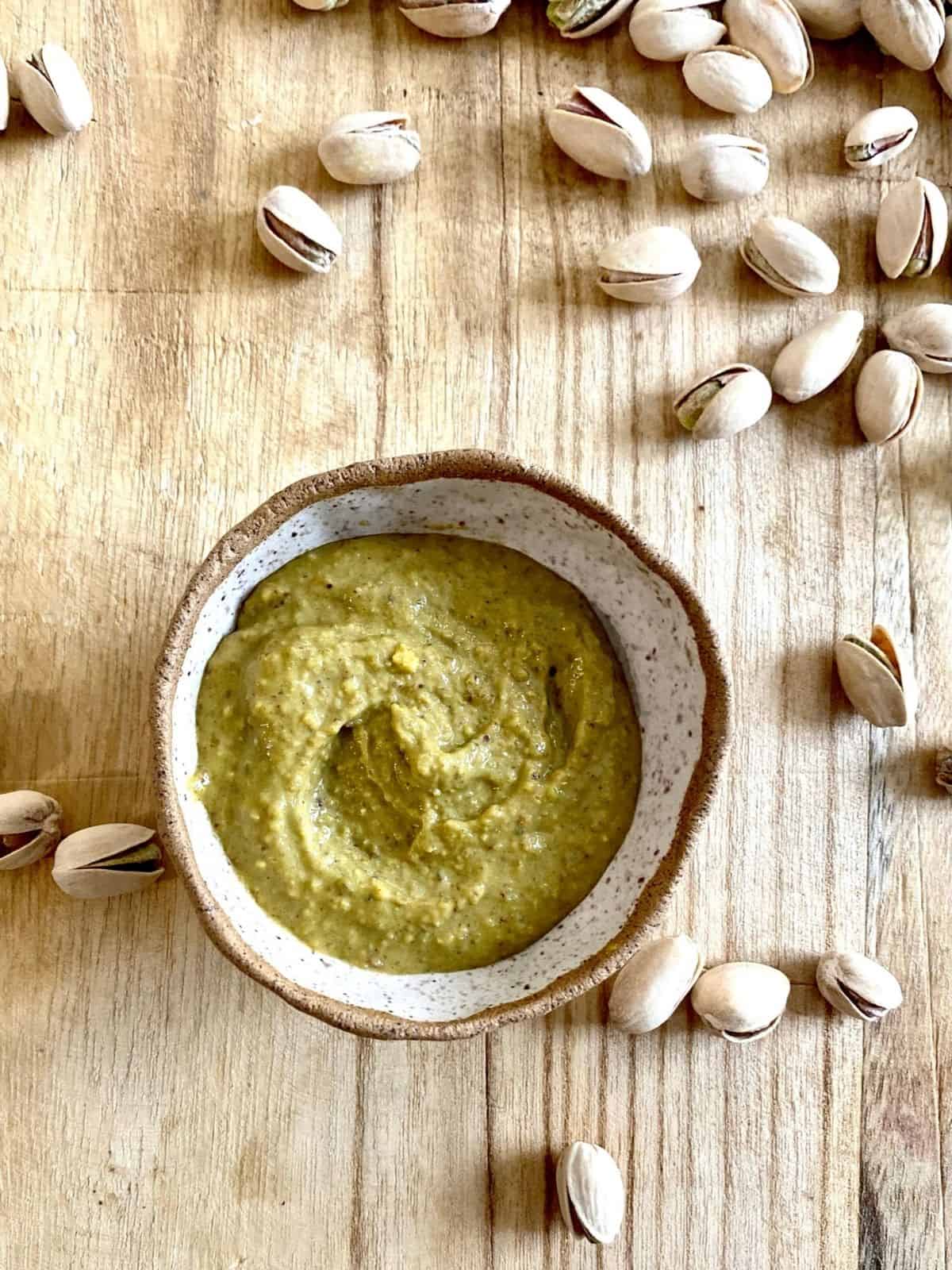 pistachio butter in small bowl surrounded by in-shell pistachios