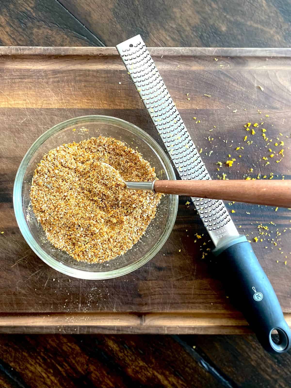 bowl of citrus dry rub with spoon on wood board next to microplane