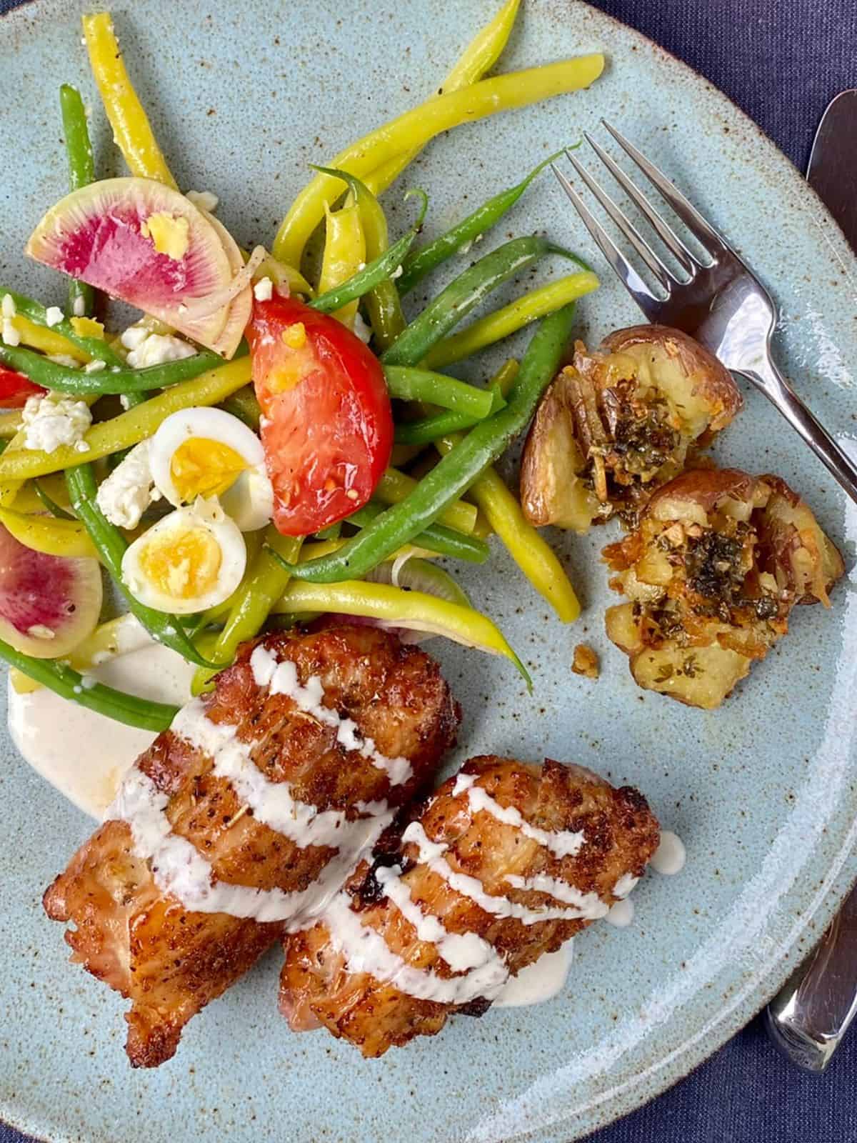 crispy citrus rubbed chicken wangs with creamy feta sauce on blue plateon plate with green bean and quail egg salad and crispy smashed redskin potatoes