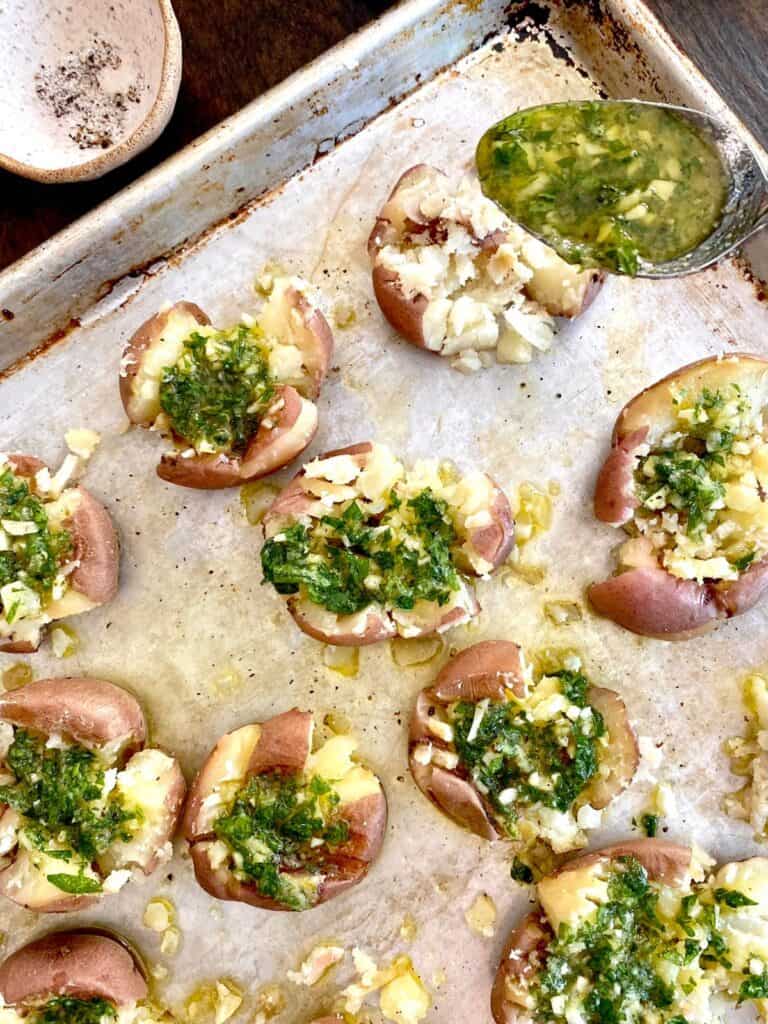 spoonful of garlicky olive oil being drizzled on smashed redskin potatoes