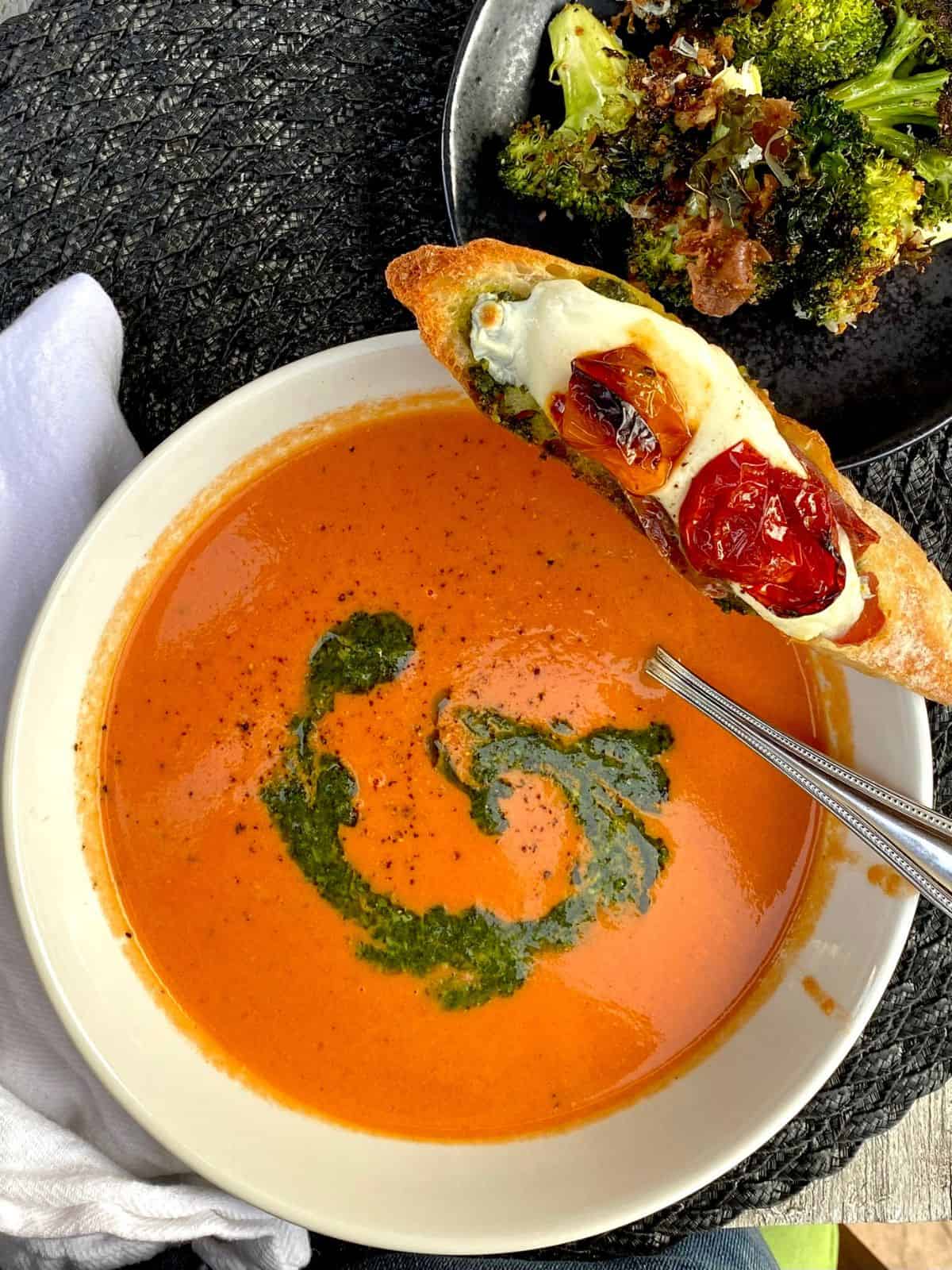 bowl of tomato soup swirled with pesto with caprese crostini resting on side of bowl
